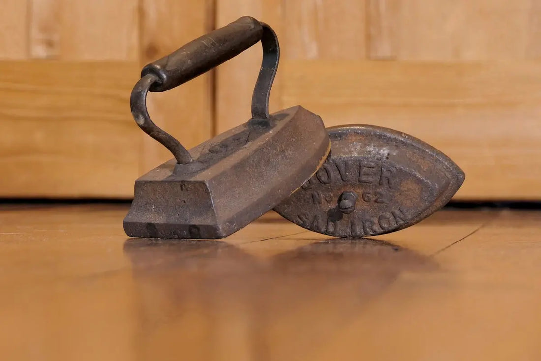 Two antique cast iron clothes irons on wooden floor.