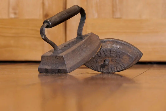 Two antique cast iron clothes irons on wooden floor.